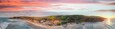 A coastal landscape with a beach, rolling hills, and a sunset.