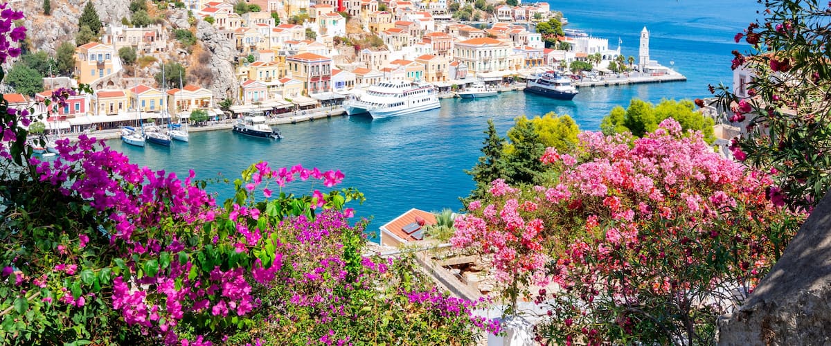 A coastal village with colorful buildings, a harbor with boats, and a mountain backdrop.