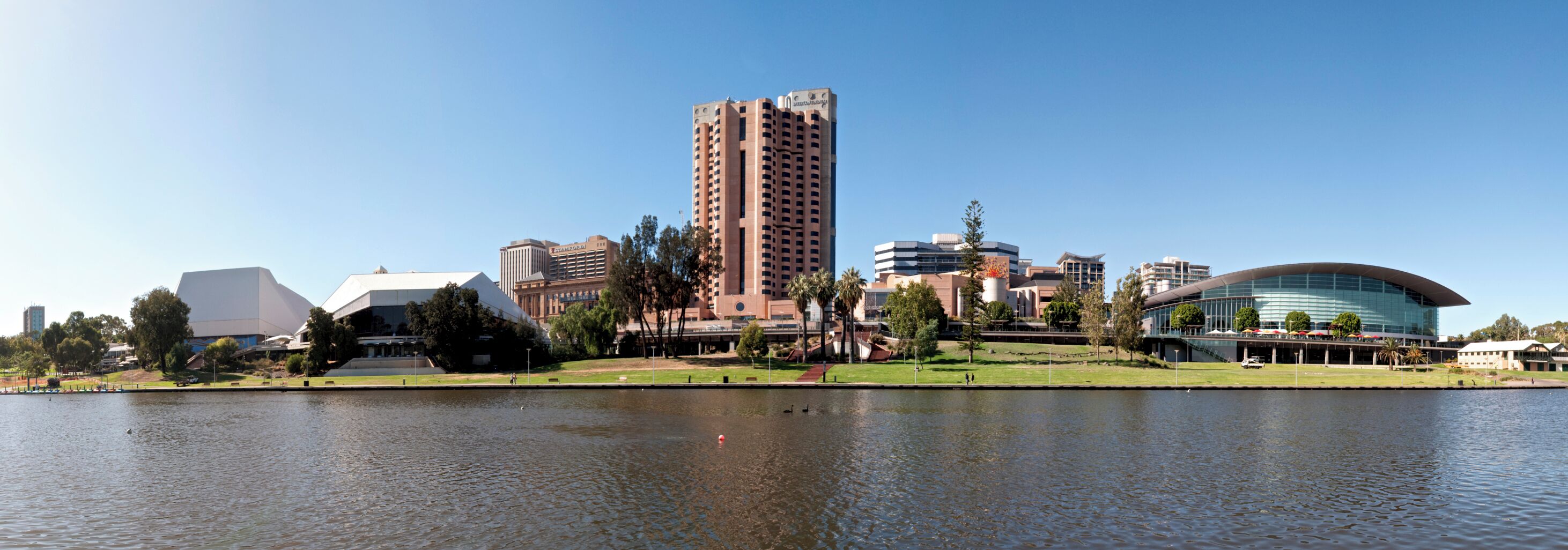 A cityscape with a prominent tall building, a modern curved building, and a body of water in the foreground.