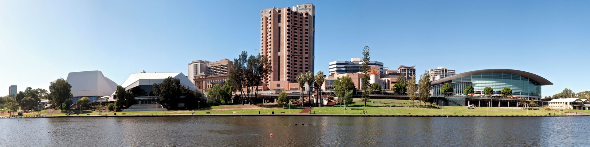 A cityscape with a prominent tall building, a modern curved building, and a body of water in the foreground.