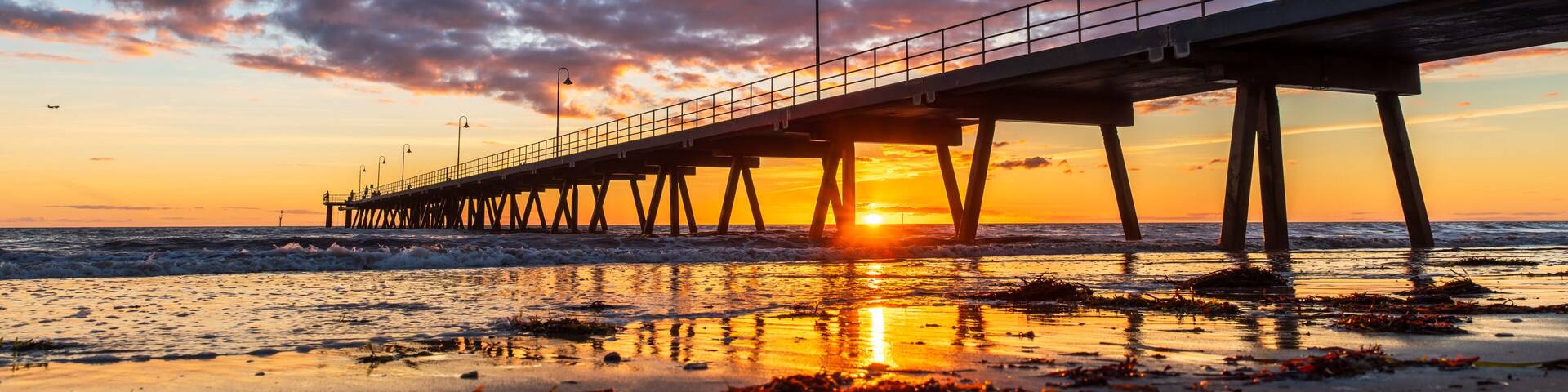 Glenelg jetty with people silhouettes standing still whicle sun dips beyond the oceanat Glenelg Beach, South Australia