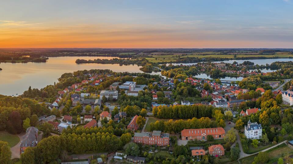 A town by a lake at sunset with a prominent church and a castle.