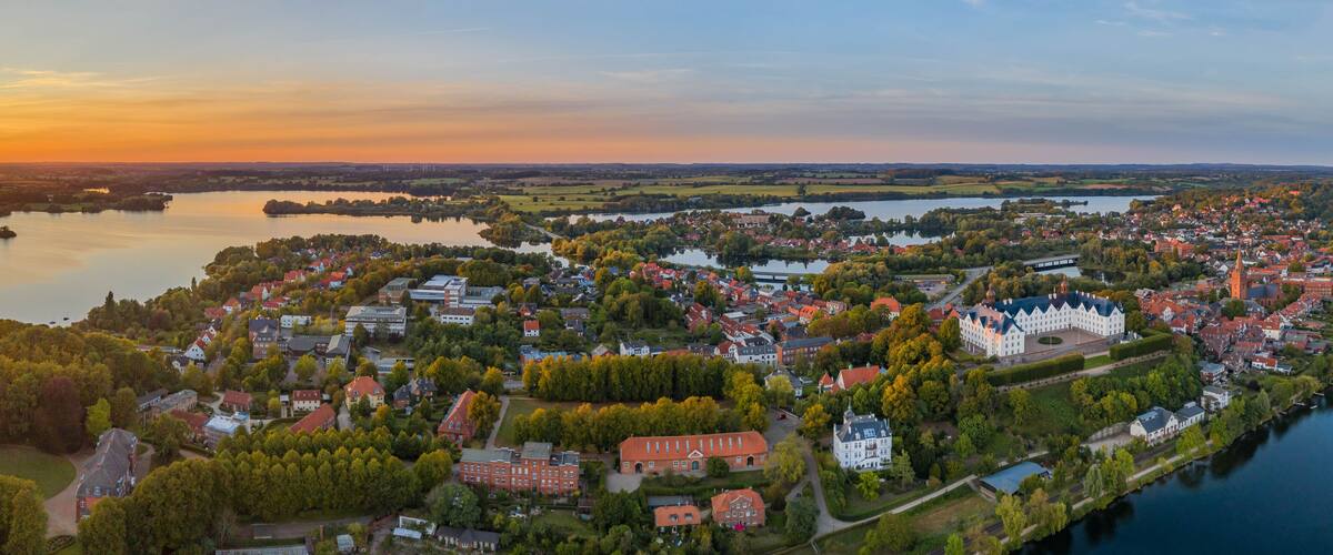 A town by a lake at sunset with a prominent church and a castle.