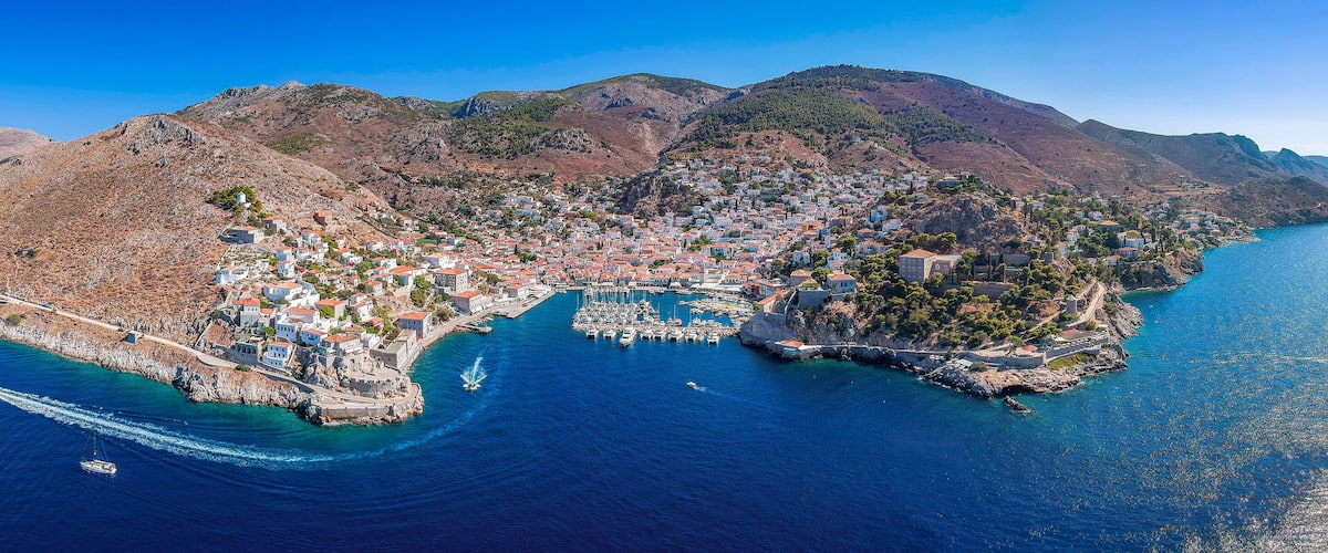 An aerial view of a coastal town with a harbor, surrounded by mountains and clear blue waters.
