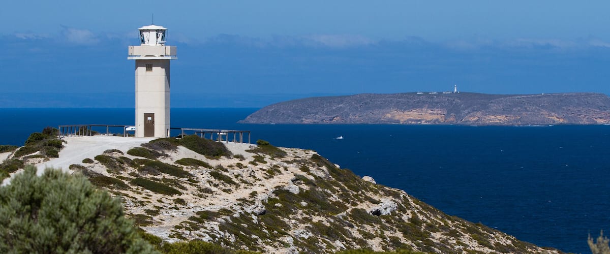A lighthouse on a rocky hill with a clear view of the ocean and a distant island.