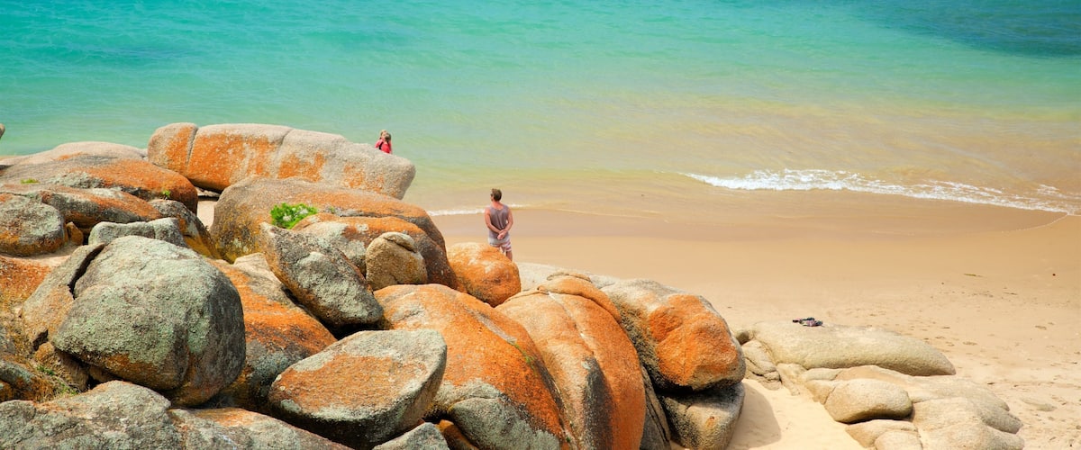 A beach with large orange rocks and a person standing on the sand.