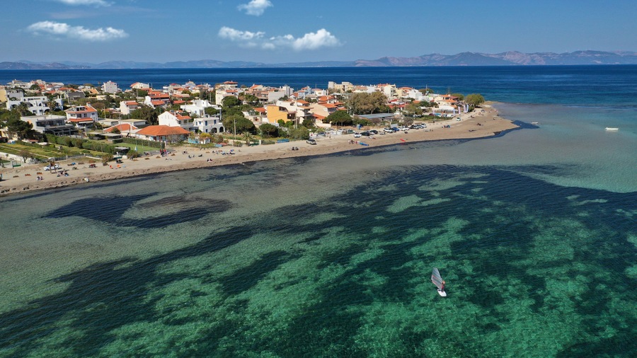 Un pueblo costero con aguas turquesas cristalinas, una playa arenosa y un velero.