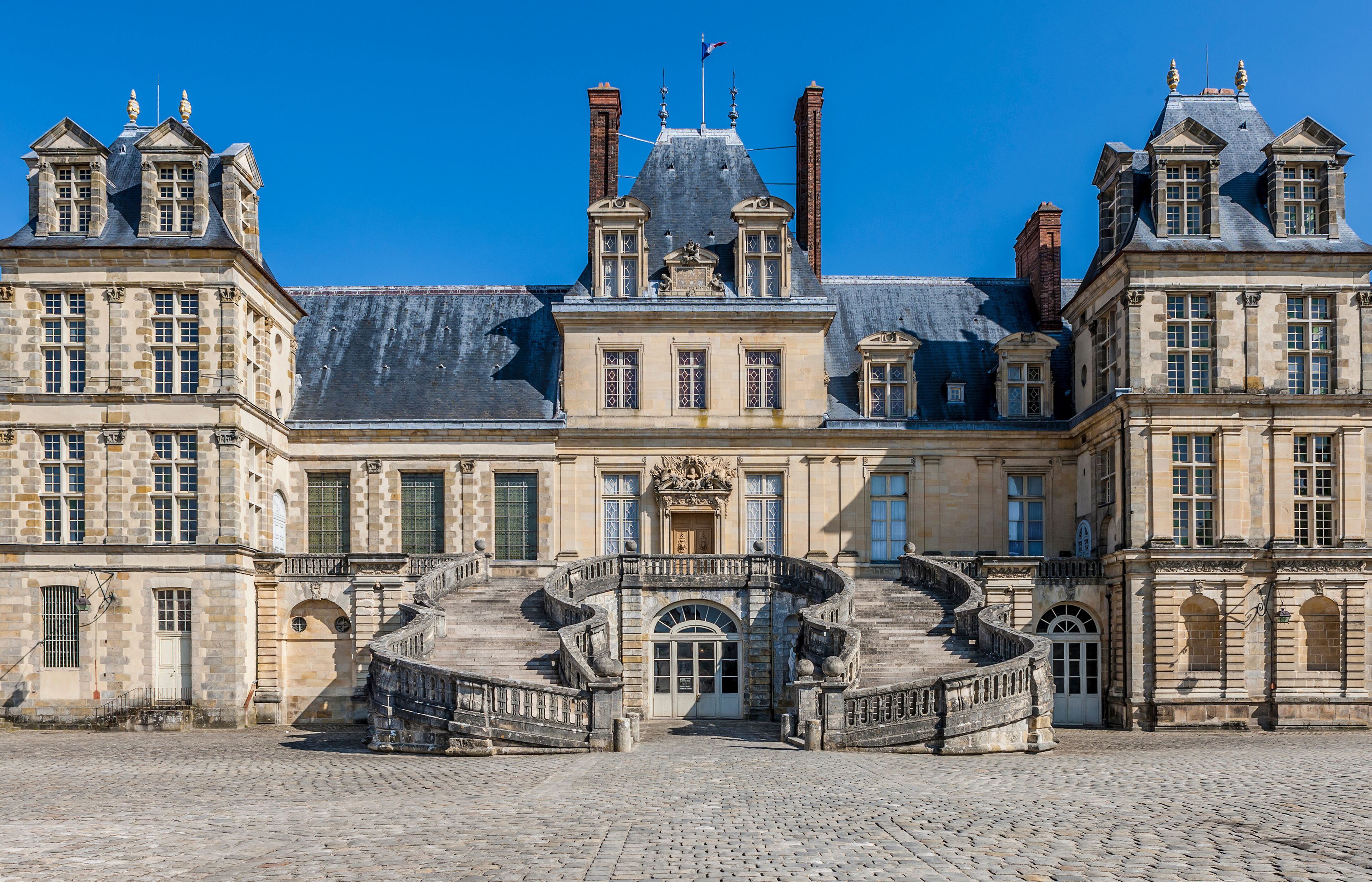 A historic building with a grand entrance, a stone staircase, and a clear blue sky.