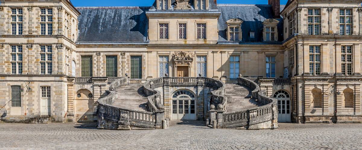 A historic building with a grand entrance, a stone staircase, and a clear blue sky.