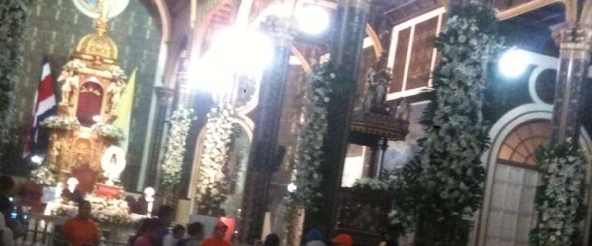 An ornate church interior with high arched ceilings, a central altar, and floral decorations.