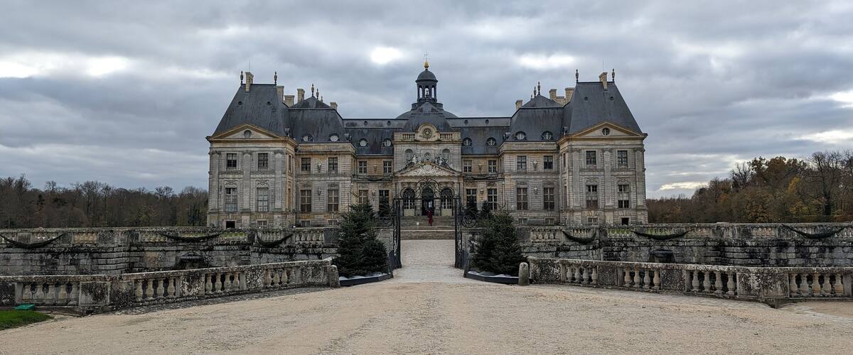 A large, historic building with a symmetrical facade, a central dome, and a statue in front.