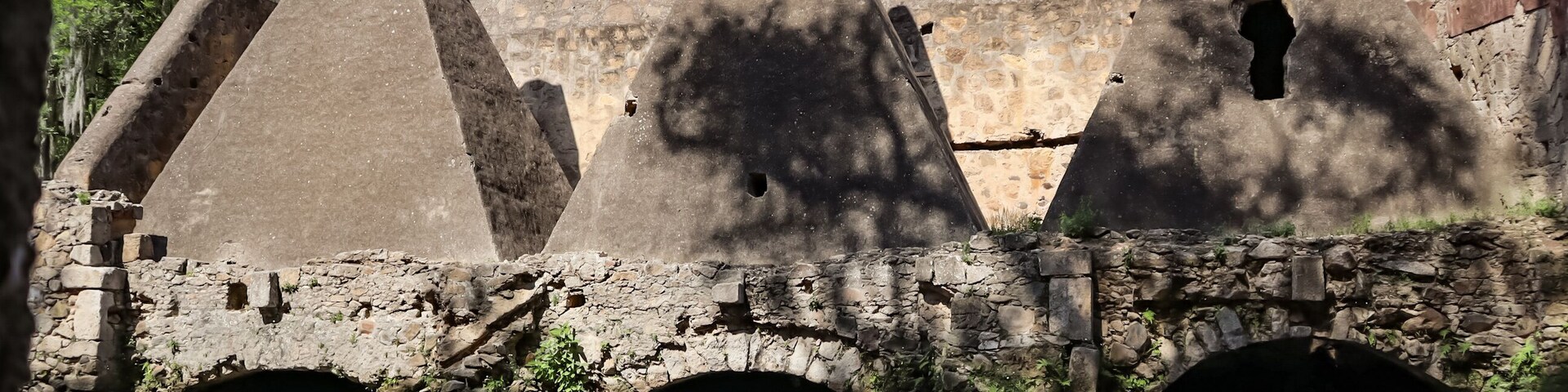 Antiguas estructuras de piedra con techos cónicos y un puente de piedra sobre una superficie acuática que refleja el entorno.