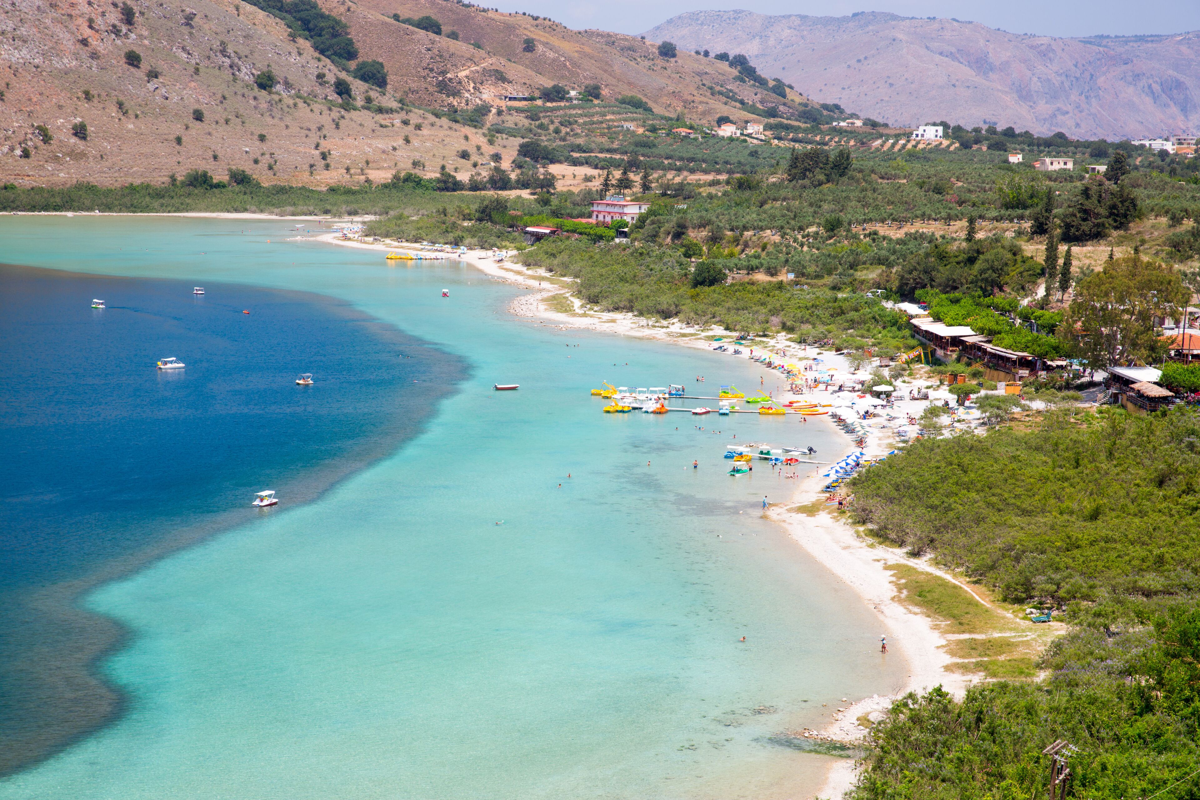 A coastal town with a beach, boats, and a mountainous backdrop.