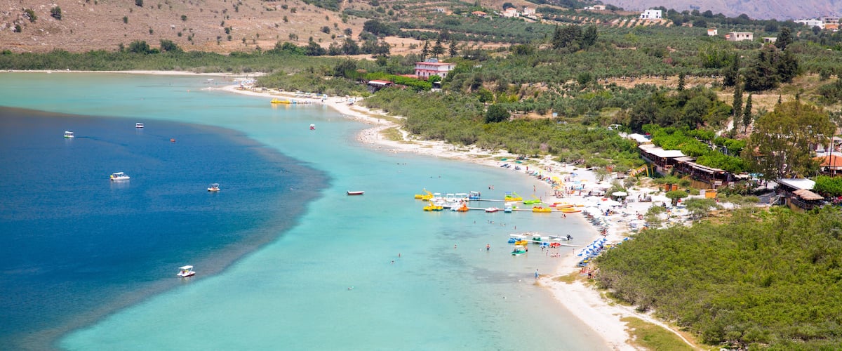 A coastal town with a beach, boats, and a mountainous backdrop.