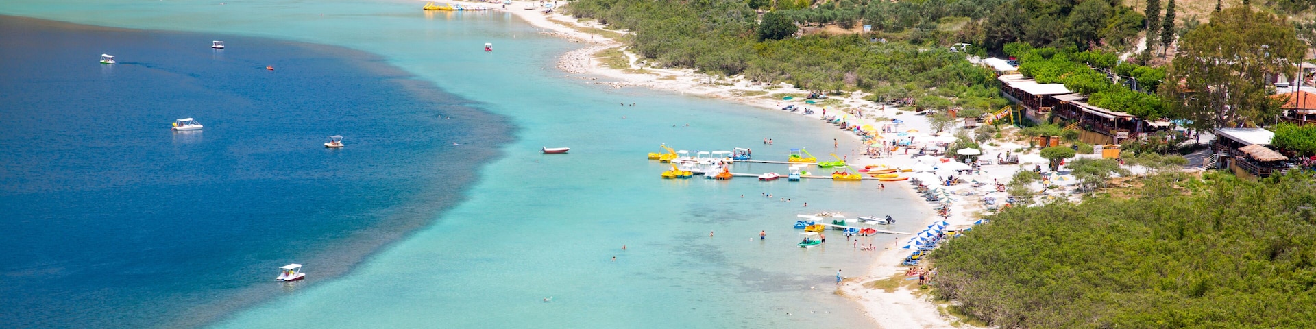A coastal town with a beach, boats, and a mountainous backdrop.