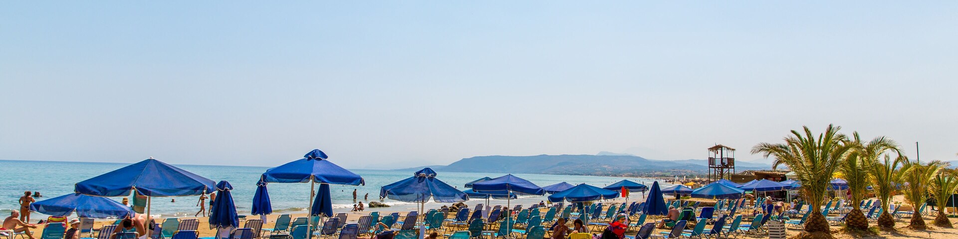 Uma praia com fileiras de guarda-sóis azuis e espreguiçadeiras.