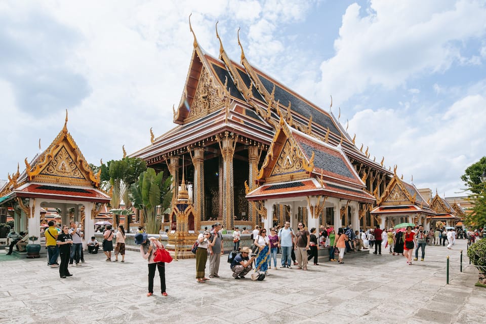 A traditional Thai temple with ornate golden roofs and columns, surrounded by tourists.
