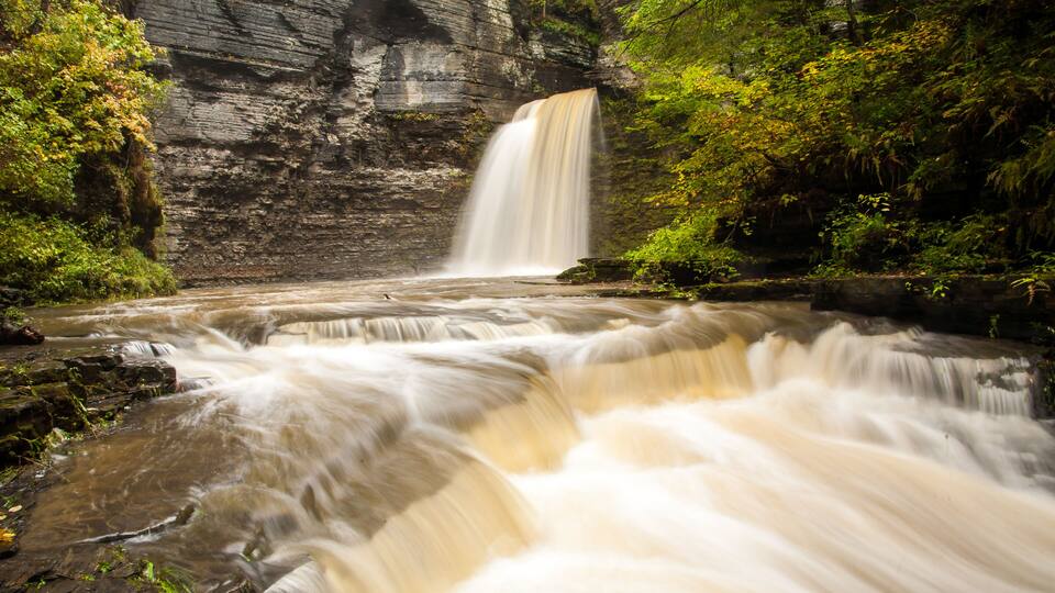 A waterfall cascading over a rocky cliff surrounded by lush greenery.