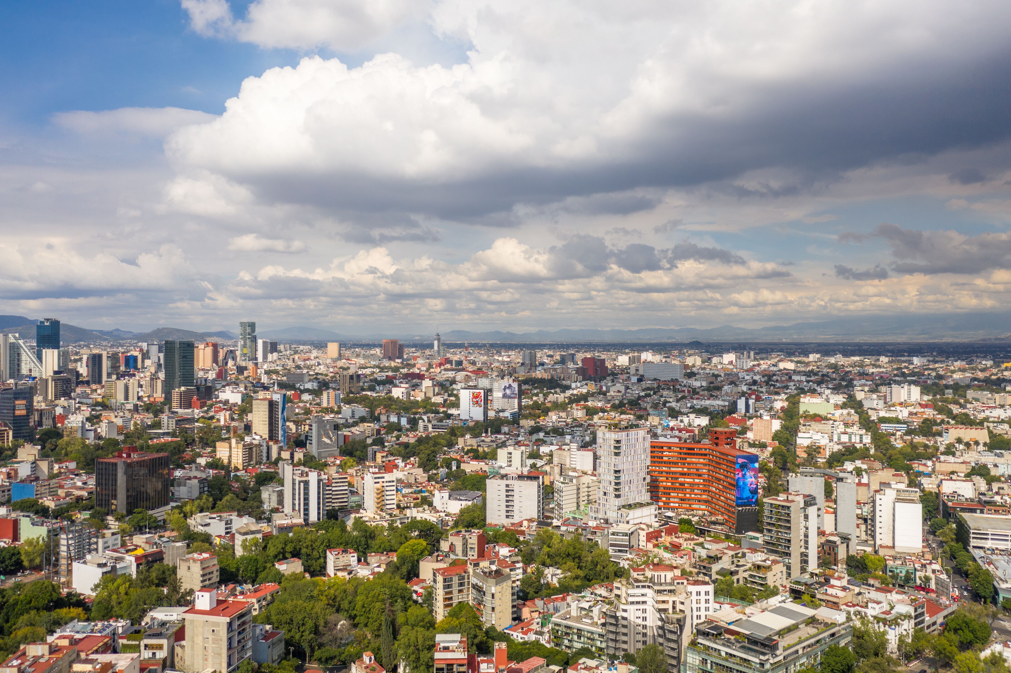 A cityscape with a mix of modern and older buildings, a prominent billboard, and a cloudy sky.