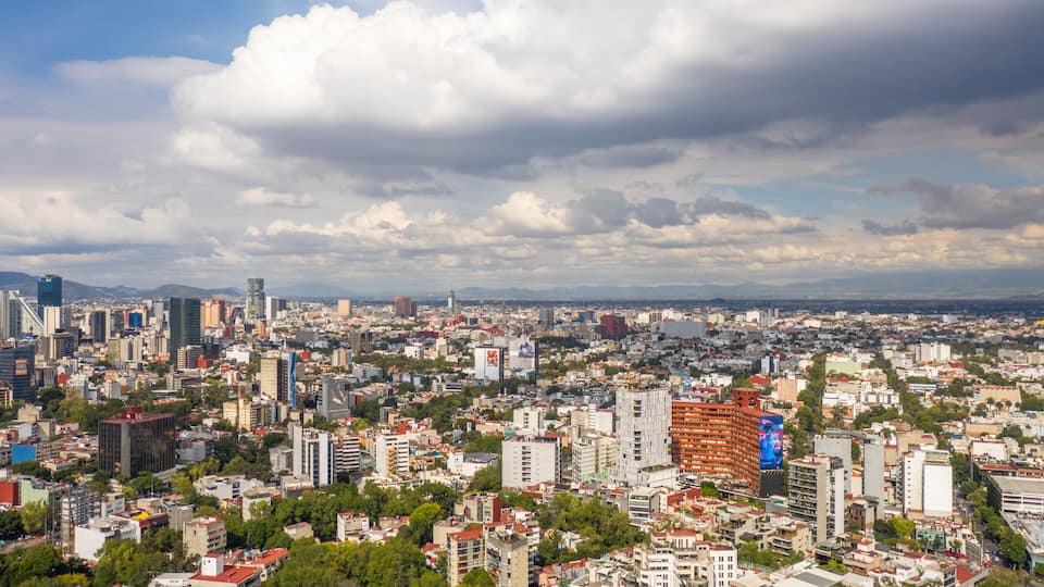 A cityscape with a mix of modern and older buildings, a prominent billboard, and a cloudy sky.