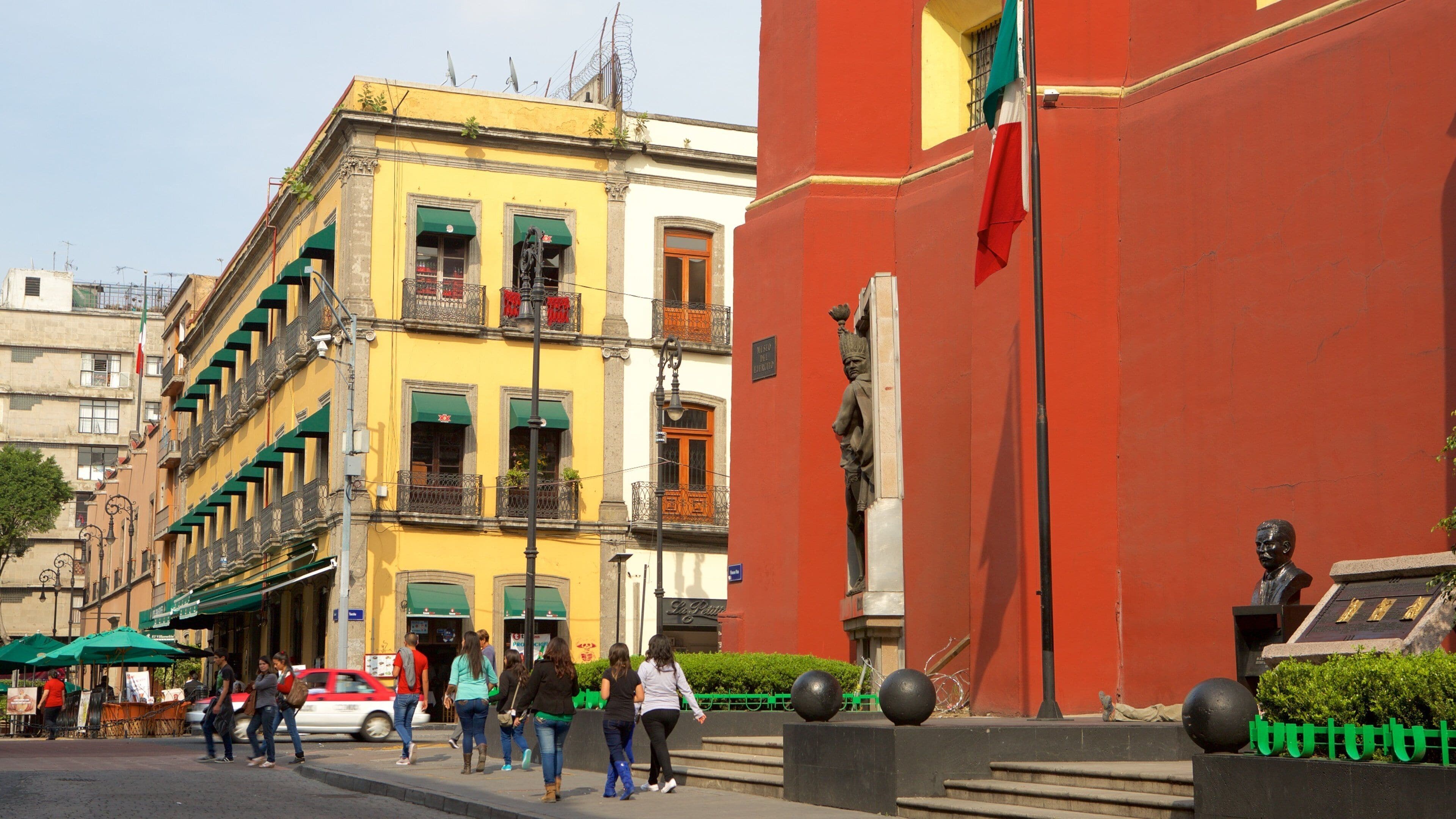 Uma rua com edifícios coloridos, pedestres e uma estátua.