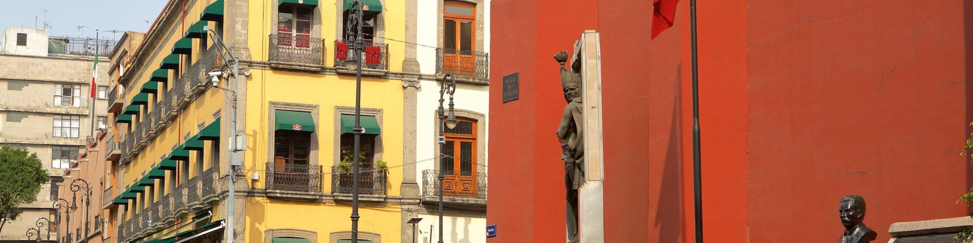 Uma rua com edifícios coloridos, pedestres e uma estátua.