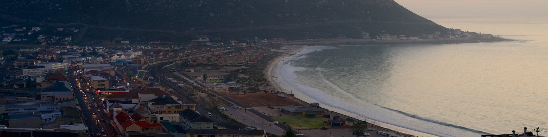 Un paisaje costero con playa, edificios urbanos y una montaña al fondo.