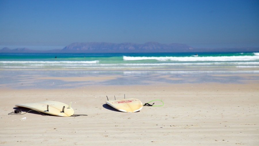 Two surfboards on a sandy beach with waves in the background and mountains in the distance.