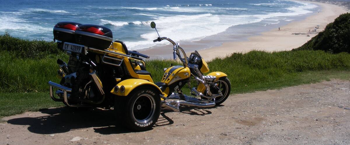 A yellow motorcycle parked on a dirt path by the ocean.