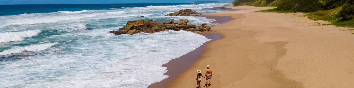 A beach with waves, a rocky outcrop, and a forested hillside.