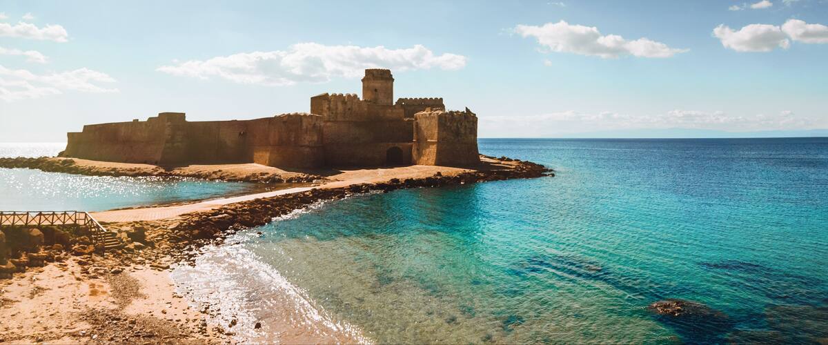 A coastal fortification with clear blue waters and a sandy beach.