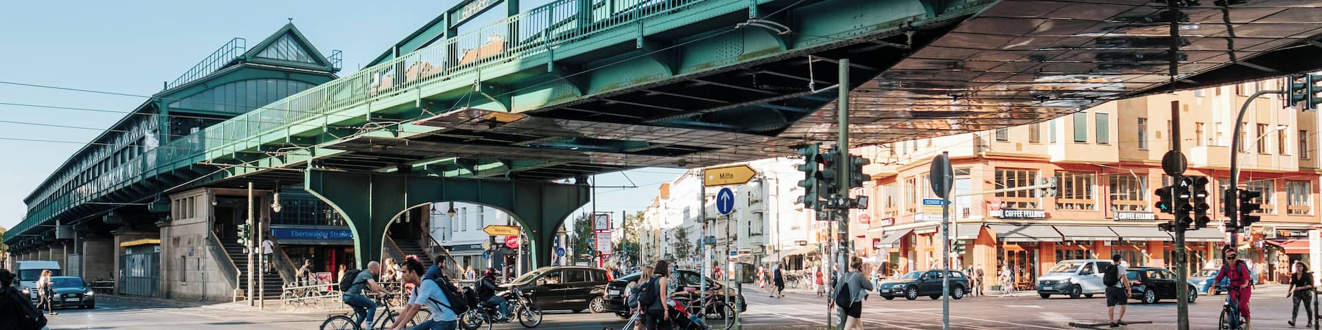A green pedestrian bridge over a busy intersection with cyclists and pedestrians.
