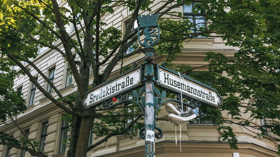 Un panneau de signalisation indiquant les noms « Sredzkistraße » et « Husemannstraße », fixé sur un poteau métallique surmonté d’une décoration héraldique.