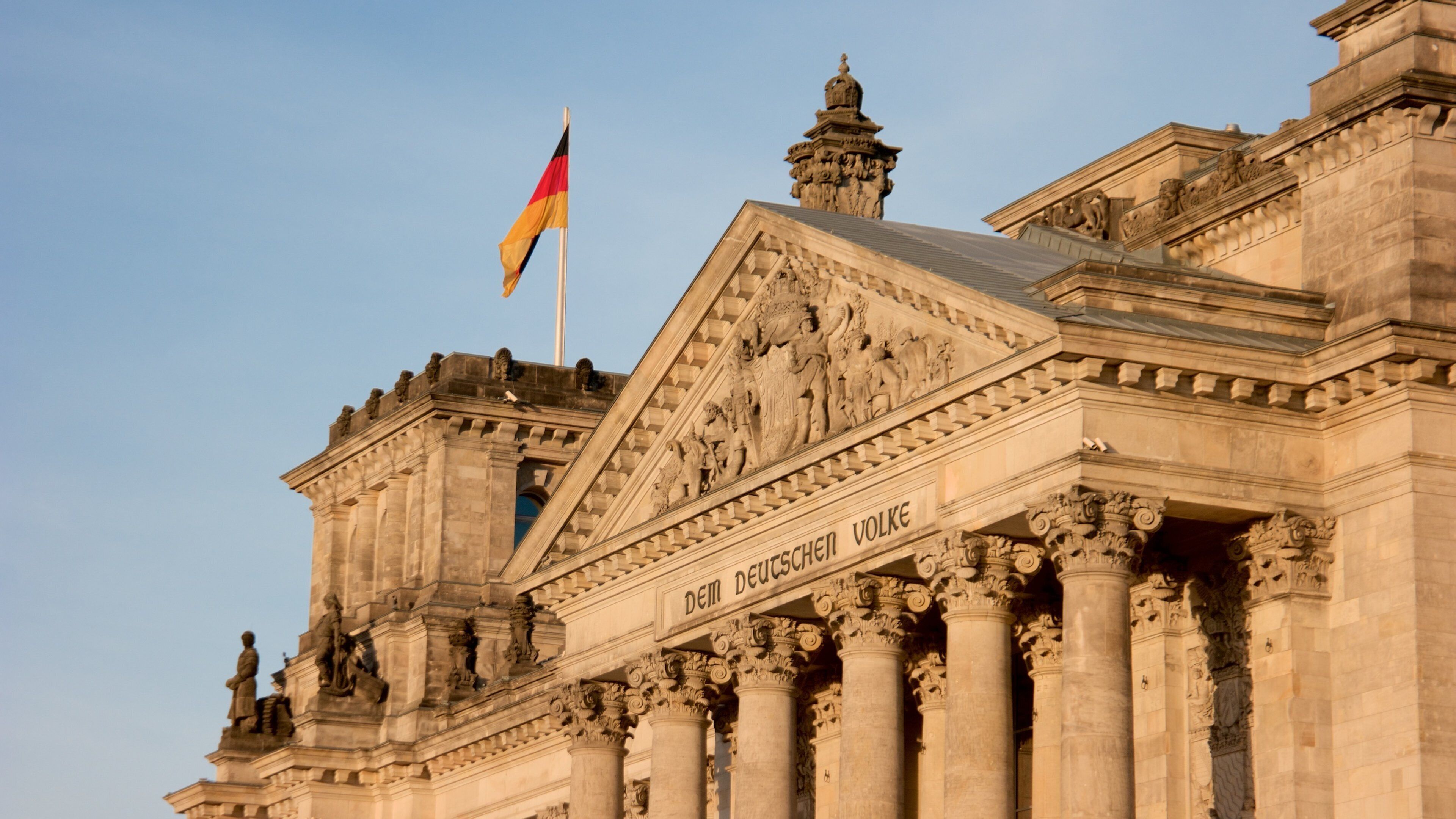Un imposant bâtiment à l’architecture classique, orné de sculptures et de colonnes travaillées, sur lequel flotte un drapeau allemand.
