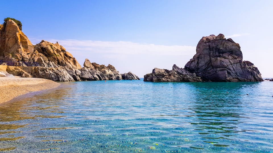 A clear coastal scene with rocky formations and calm turquoise waters.