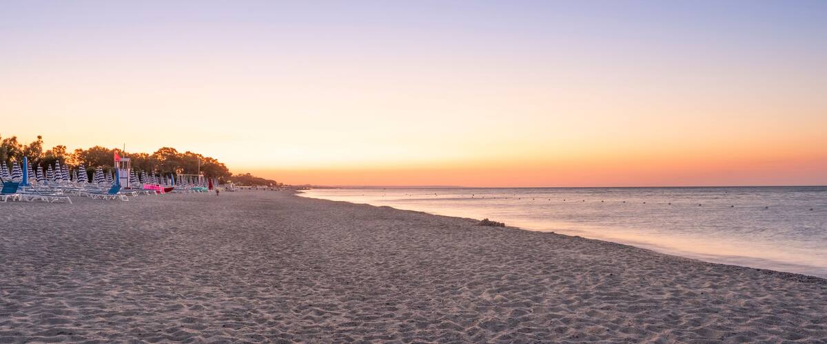 A beach with lounge chairs and umbrellas, a lifeguard tower, and a sunset over the ocean.