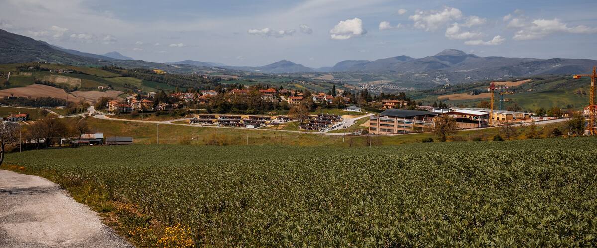 A town nestled in a valley with mountains in the background, surrounded by fields and construction cranes.