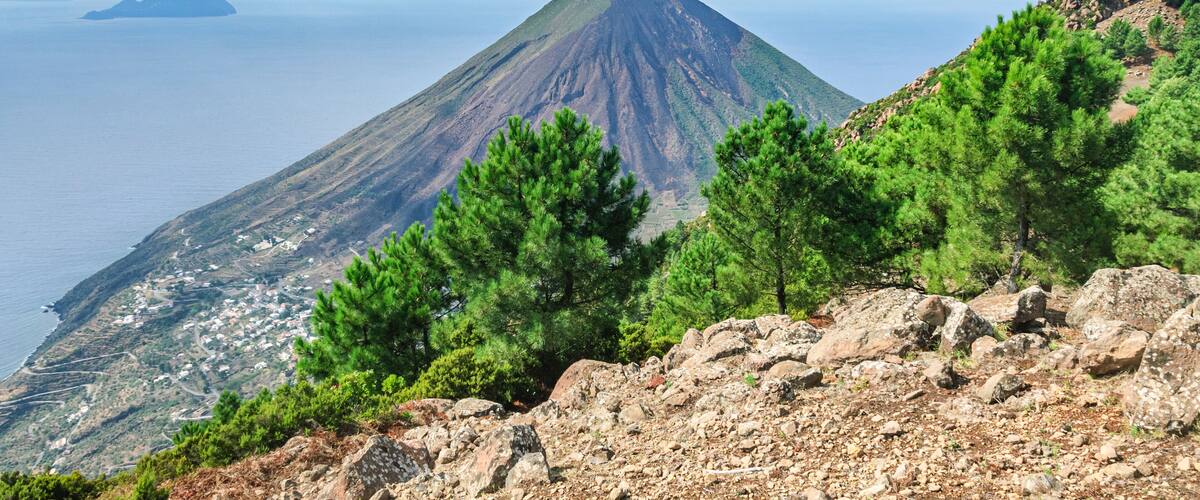 A mountain with a conical shape, a coastal town below, and a clear sky.