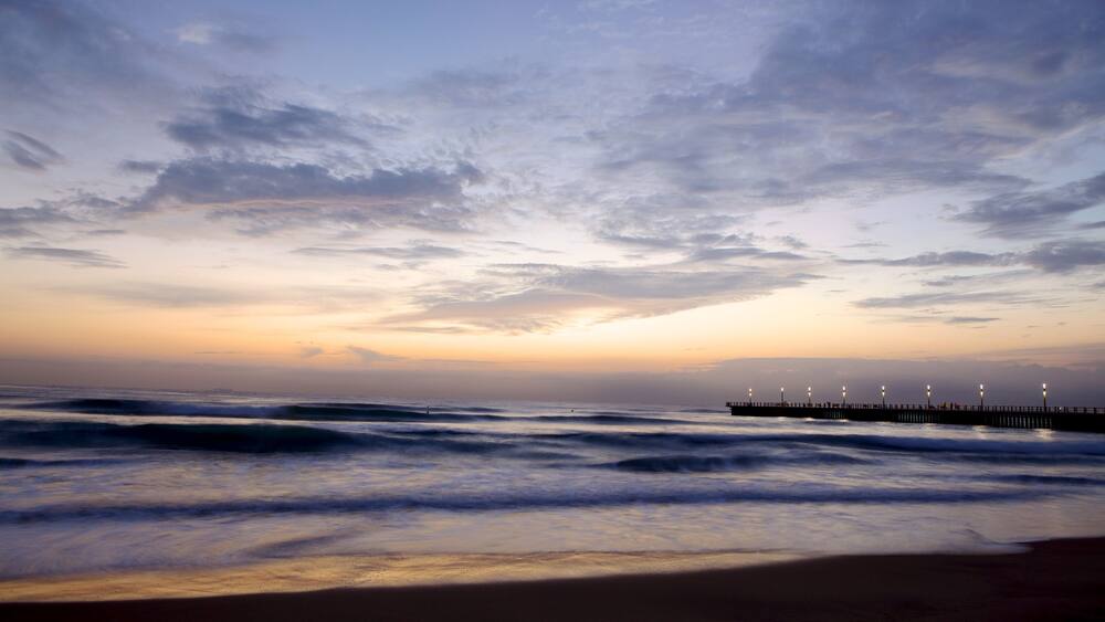 A beach with waves and a pier with lights.