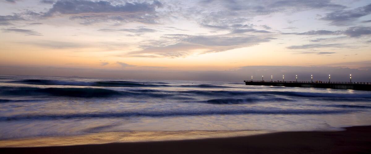 A beach with waves and a pier with lights.
