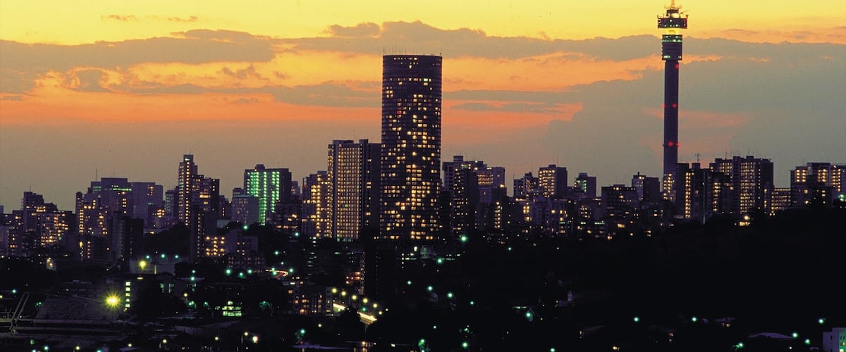 A city skyline at dusk with illuminated buildings and a prominent tower.