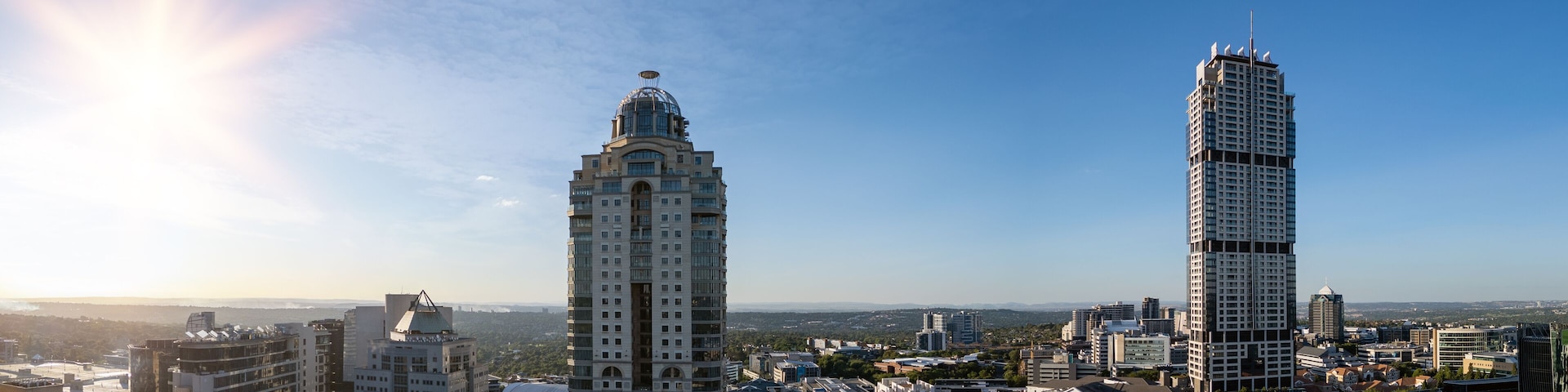 Dois arranha-céus imponentes, um edifício com cúpula e uma paisagem urbana densa sob um céu limpo.