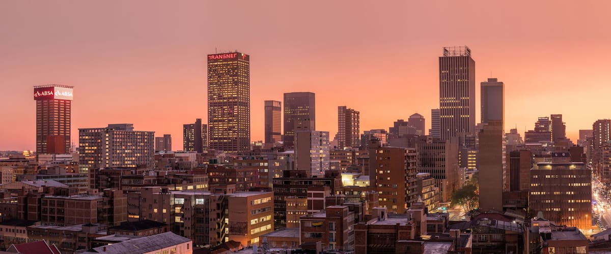 A cityscape at dusk with illuminated buildings and a prominent skyscraper labeled "ABSA".