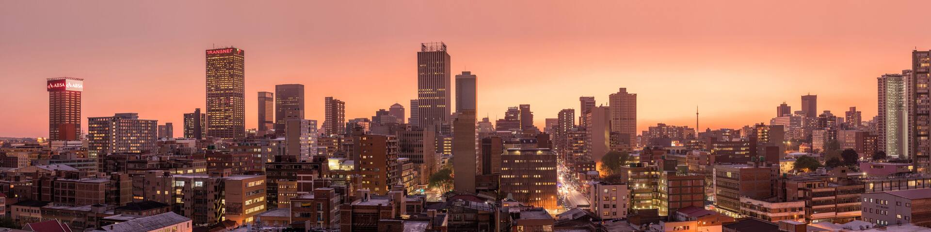 A cityscape at dusk with illuminated buildings and a prominent skyscraper labeled "ABSA".