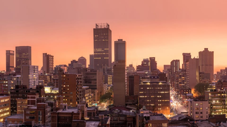 A cityscape at dusk with illuminated buildings and a prominent skyscraper labeled "ABSA".