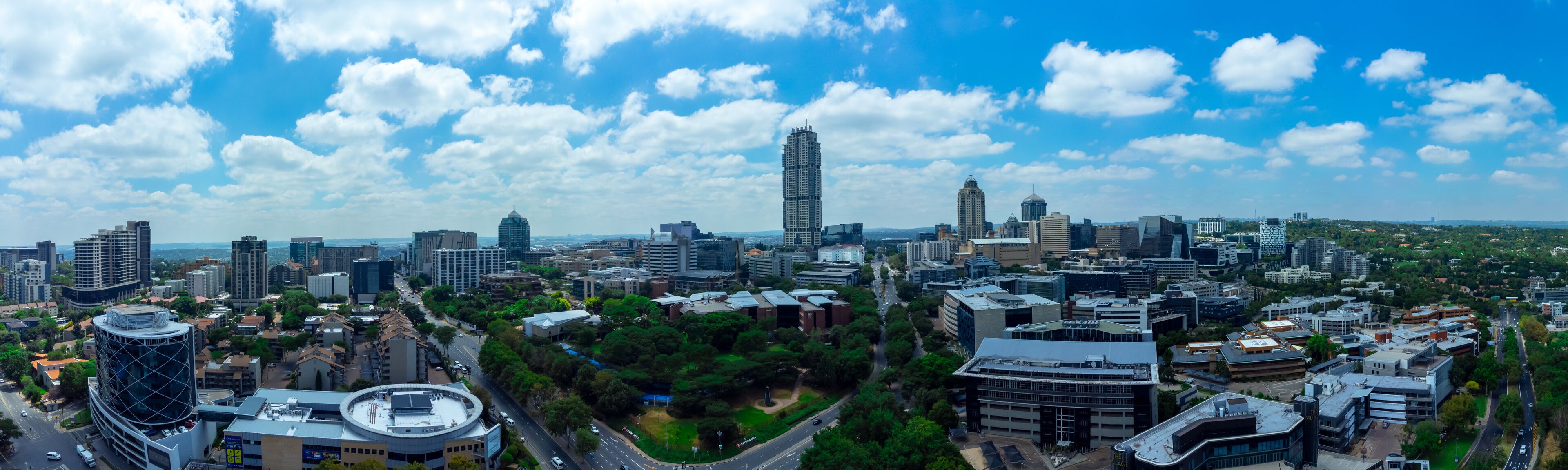 A cityscape with modern skyscrapers, a prominent tower, and a mix of greenery.