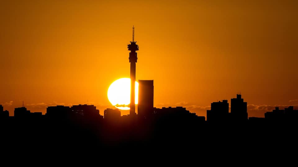 A city skyline silhouetted against a sunset with a prominent tower.