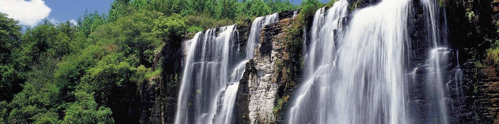 A multi-tiered waterfall cascading into a calm pool surrounded by dense green forest.
