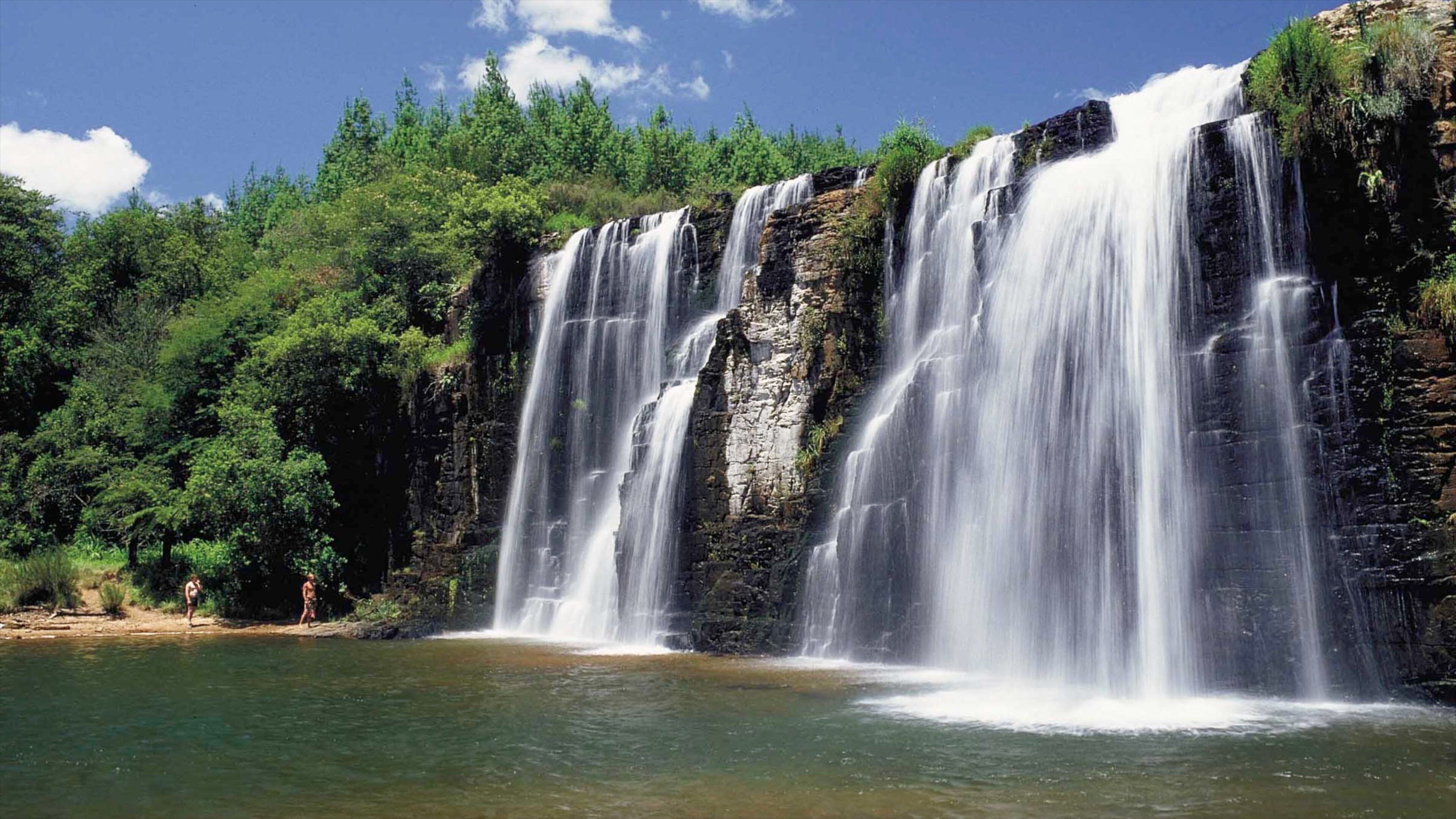 A multi-tiered waterfall cascading into a calm pool surrounded by dense green forest.