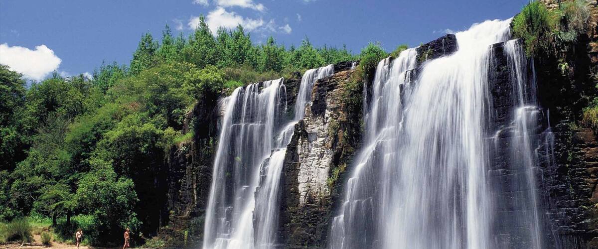 A multi-tiered waterfall cascading into a calm pool surrounded by dense green forest.